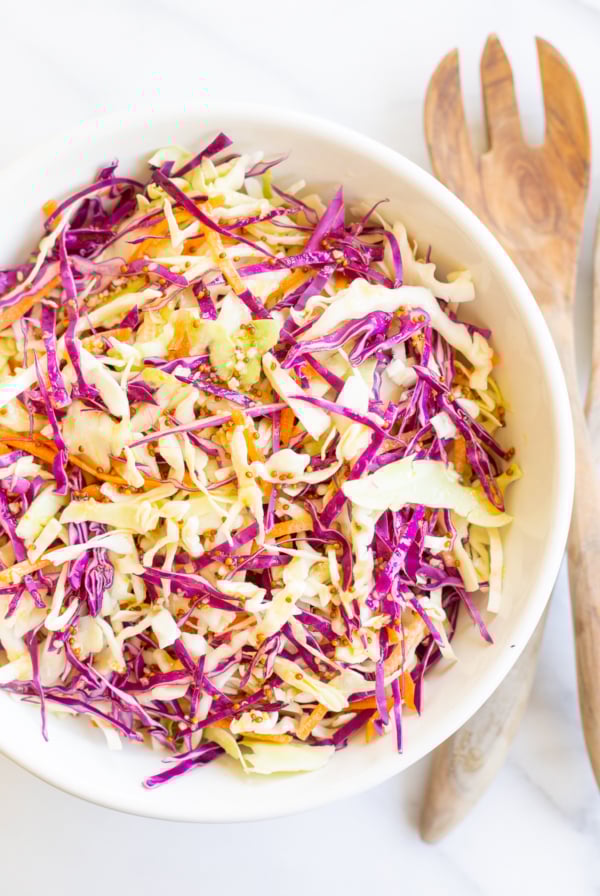 White salad bowl filled with colorful cabbage salad and wooden serving spoons.