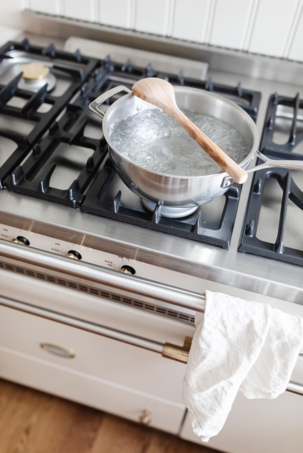 A silver pot of boiling water on a French range, with a wooden spoon placed over the top to stop water from boiling over.