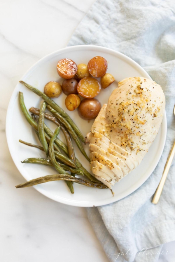 A white plate with rosemary chicken, potatoes and green beans.