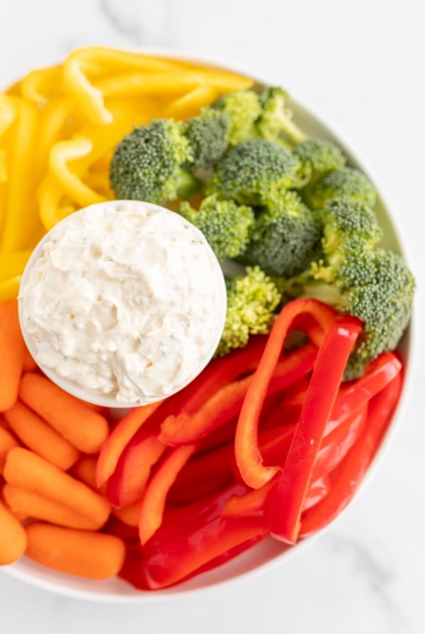 A white bowl full of veggie dip, surrounded by cut vegetables.