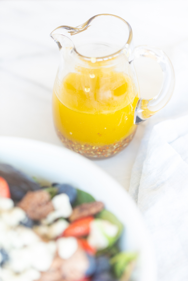A small glass pitcher full of homemade vinaigrette dressing next to a salad.